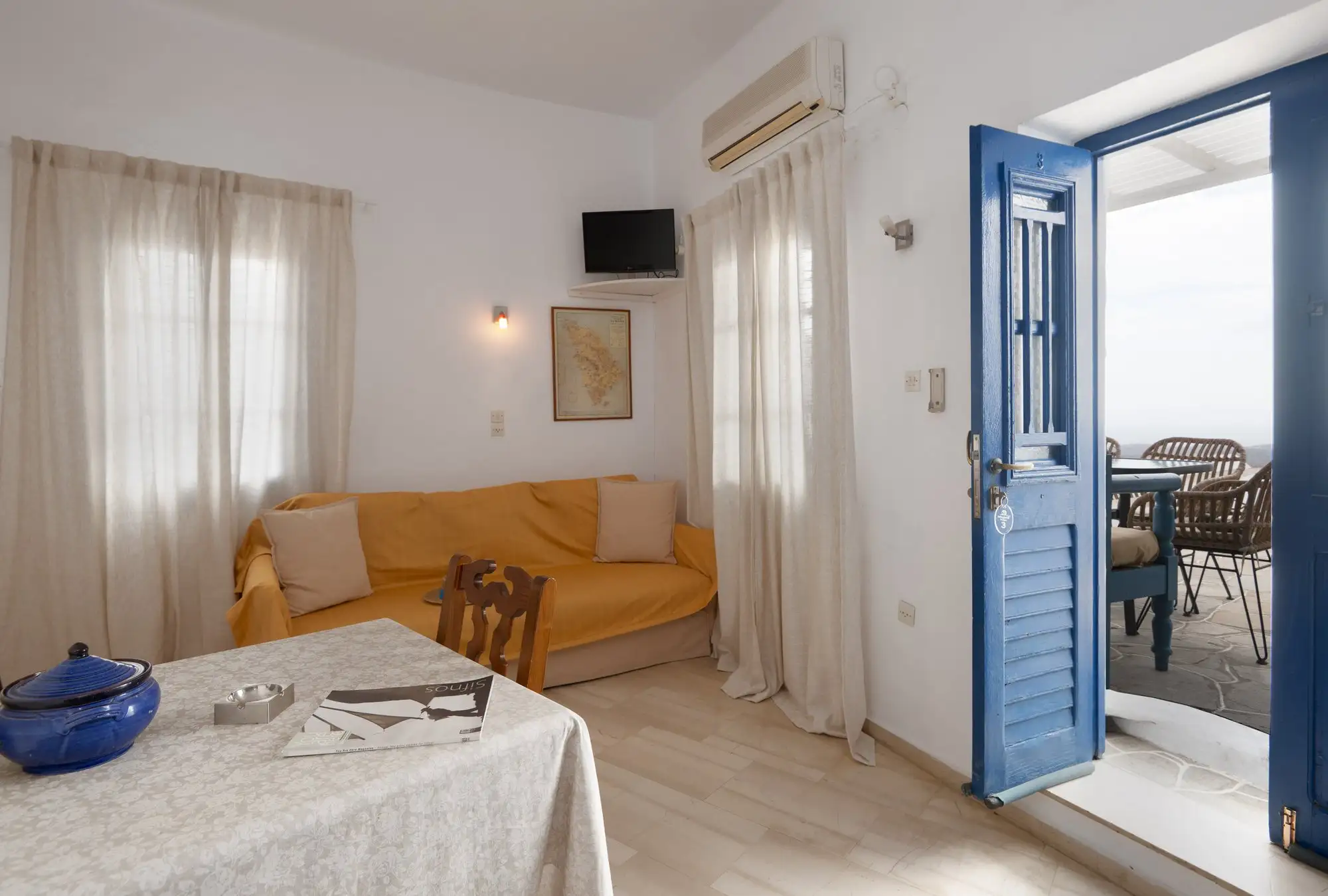 Appartement Eos : séjour avec canapé, table à manger et porte bleue vers la terrasse