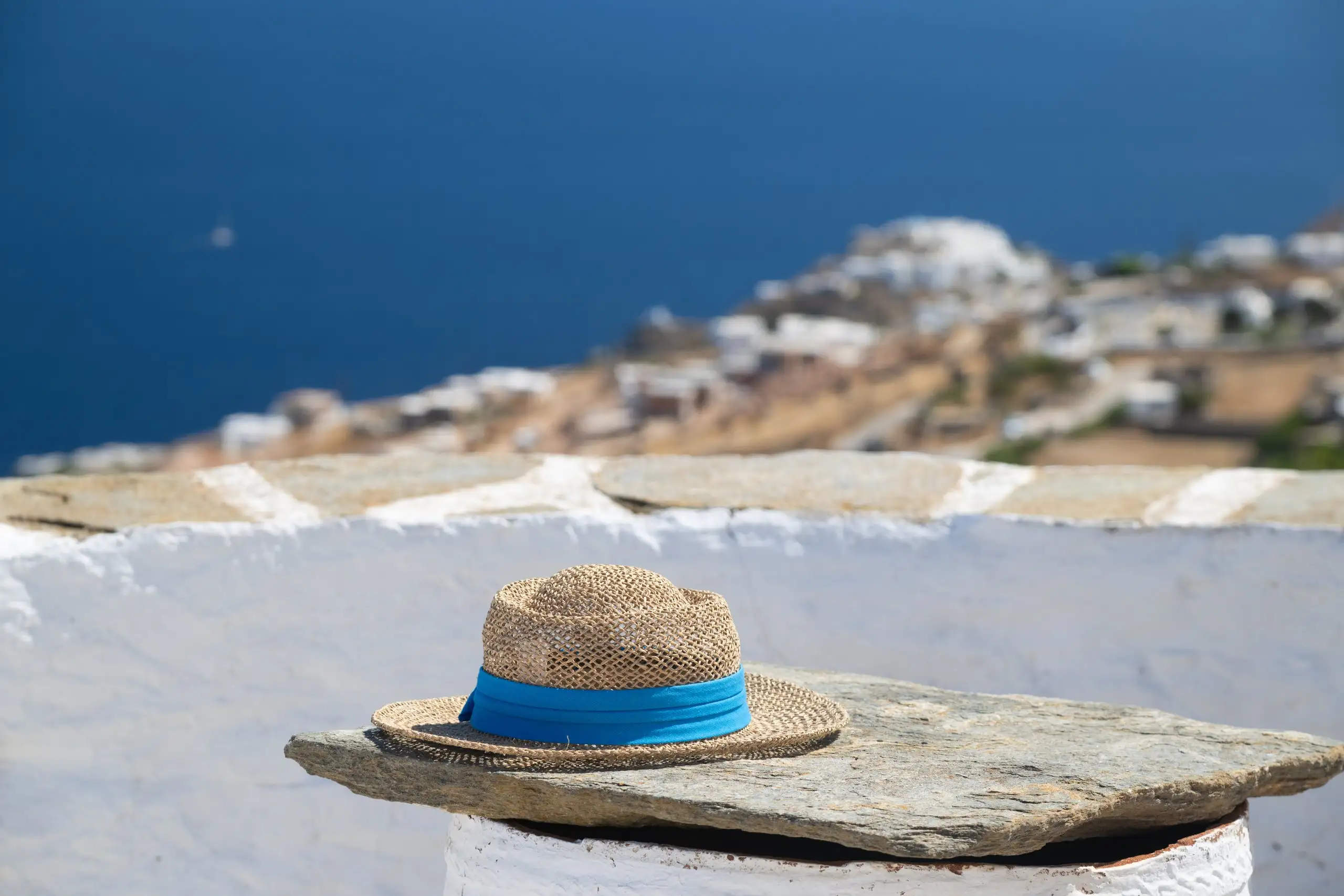 Chapeau de paille sur un muret blanchi à la chaux, avec un village de Sifnos et la mer au loin