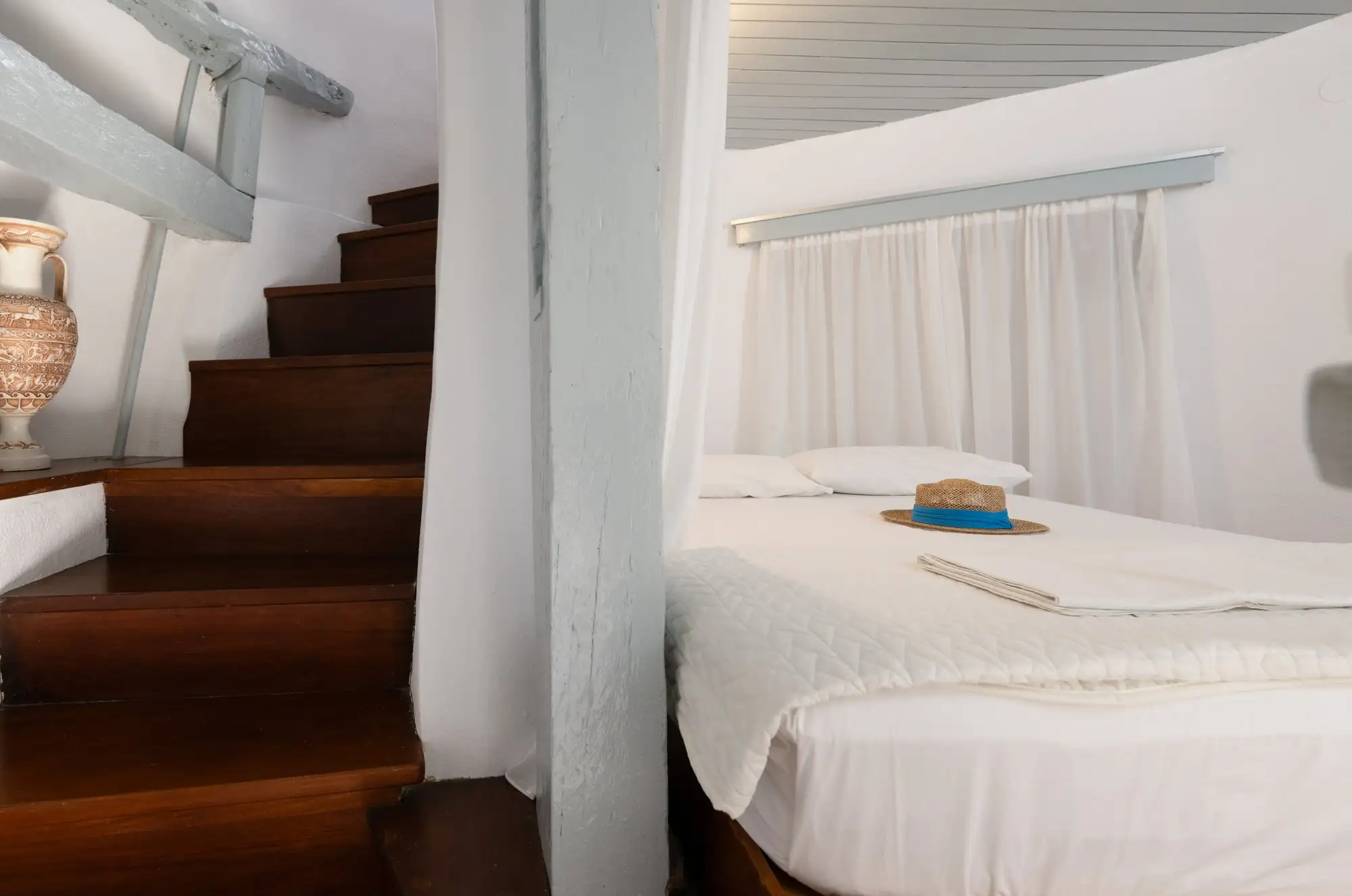L’escalier en bois et le lit du premier étage, derrière un rideau blanc