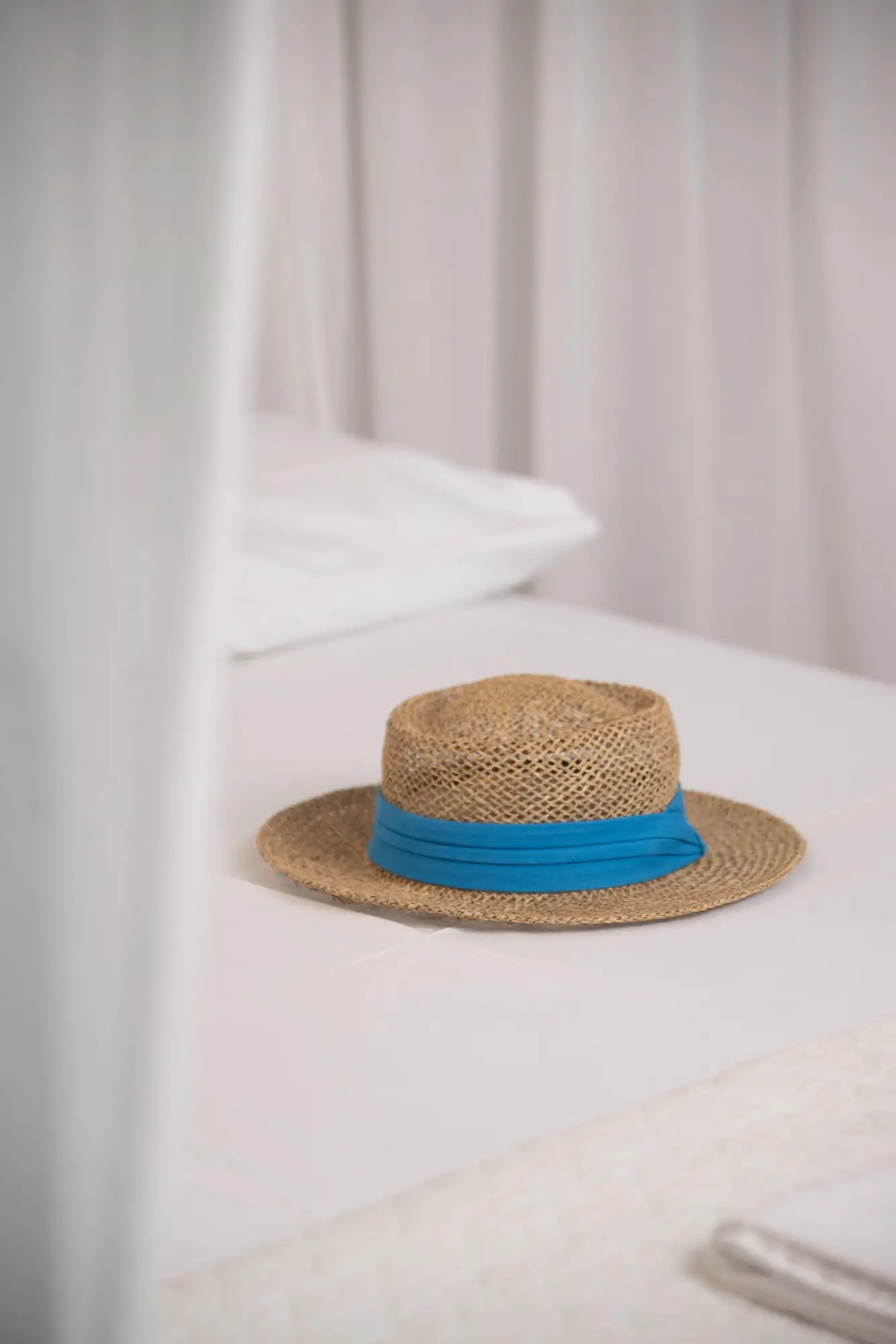 Un chapeau de paille à ruban bleu sur des draps blancs